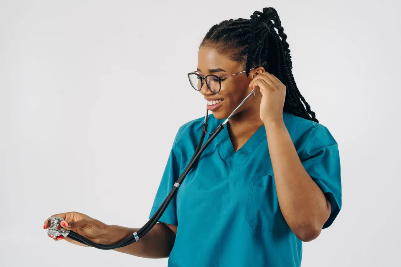 A smiling nurse in teal scrubs holding a stethoscope